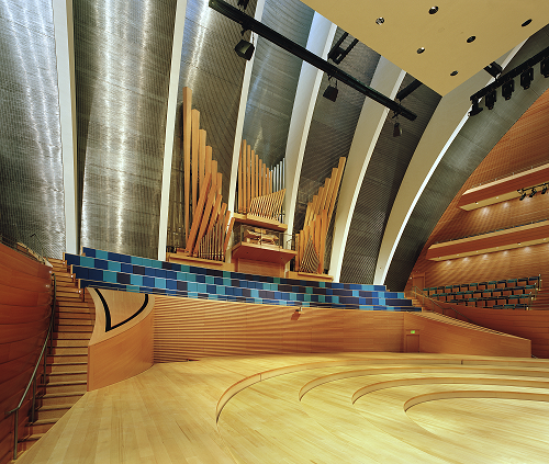 A modern concert hall with wooden seating and stage, featuring a large pipe organ and arched ceilings.