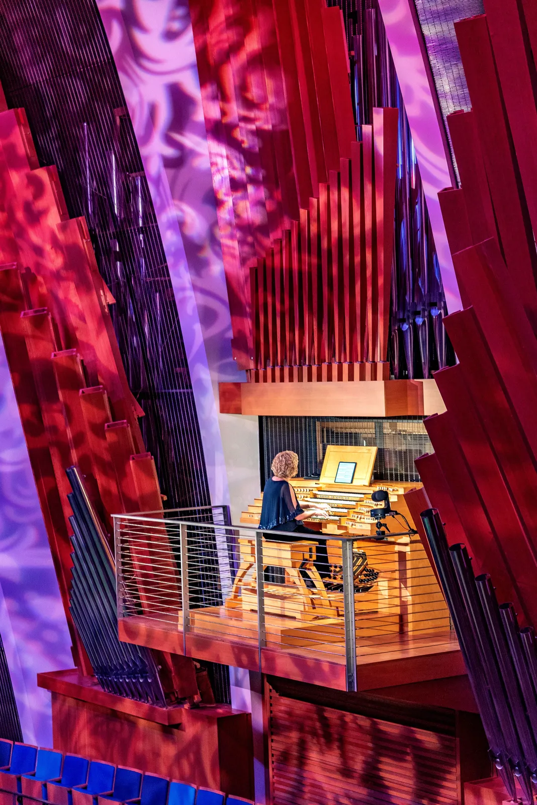 An organist playing a large pipe organ on a platform surrounded by red acoustic panels, with purple lights casting patterns on the walls, could be the perfect backdrop for an event highlighting nonprofit jobs in Kansas City.