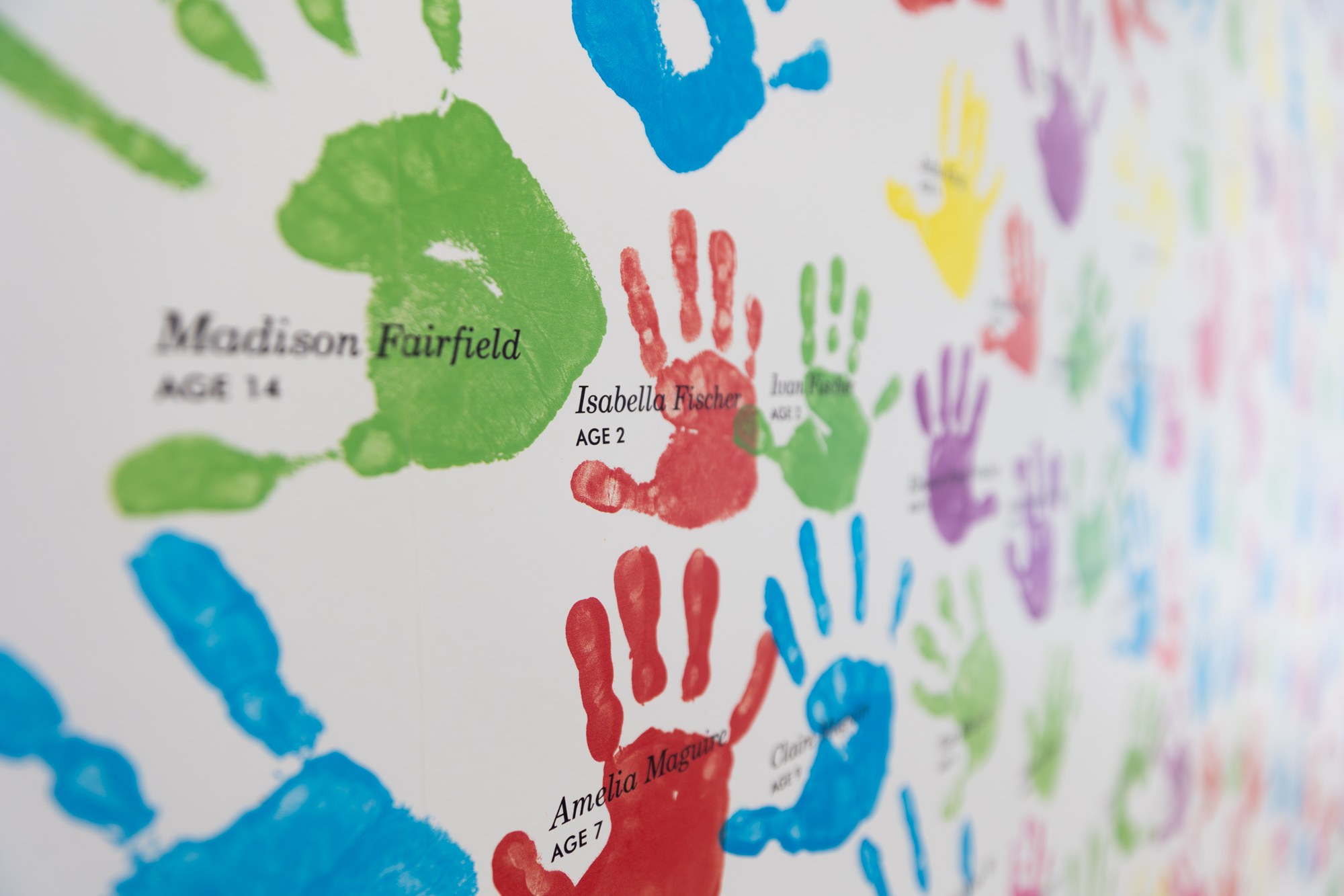 A wall featuring colorful handprints surrounds text explaining that children's handprints are donations supporting community arts, beautifully displayed at the Kauffman Center for the Performing Arts. Visitors can view this heartwarming exhibit as part of a guide to the Kauffman Center.