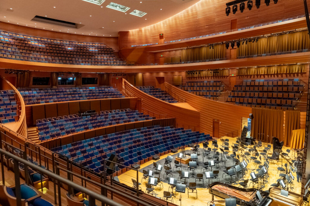 A modern concert hall with tiered seating and a stage set with musical instruments for an orchestra.