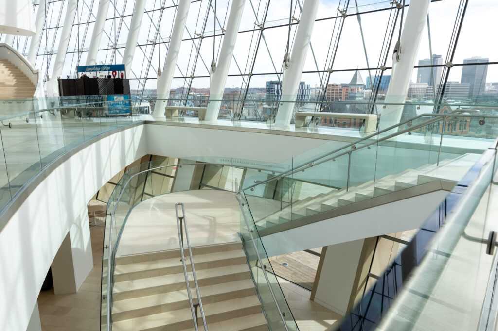 Bright, open interior space featuring curved glass railings, stairs, with large windows offering a cityscape view from the Kauffman Center.