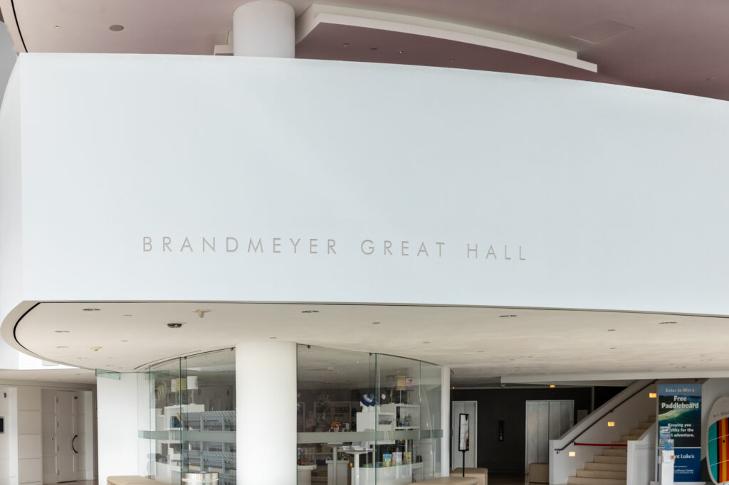 A view of the interior of Brandmeyer Great Hall, featured in the Kauffman Center, showcasing modern architectural design with a curved white wall and glass display case.