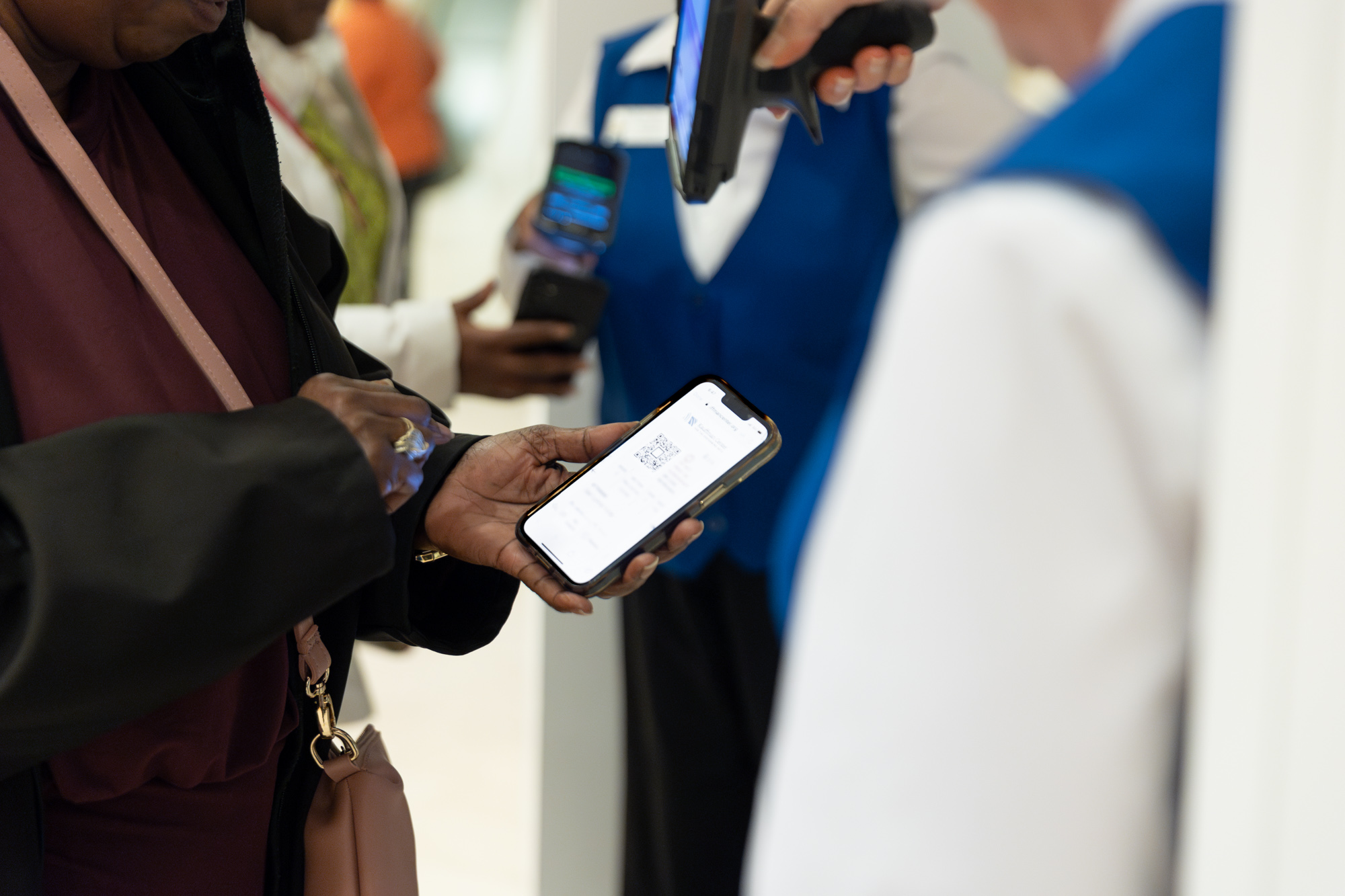 A person holding a smartphone displaying a QR code to an attendant in a blue vest for scanning, referencing the Kauffman Center.