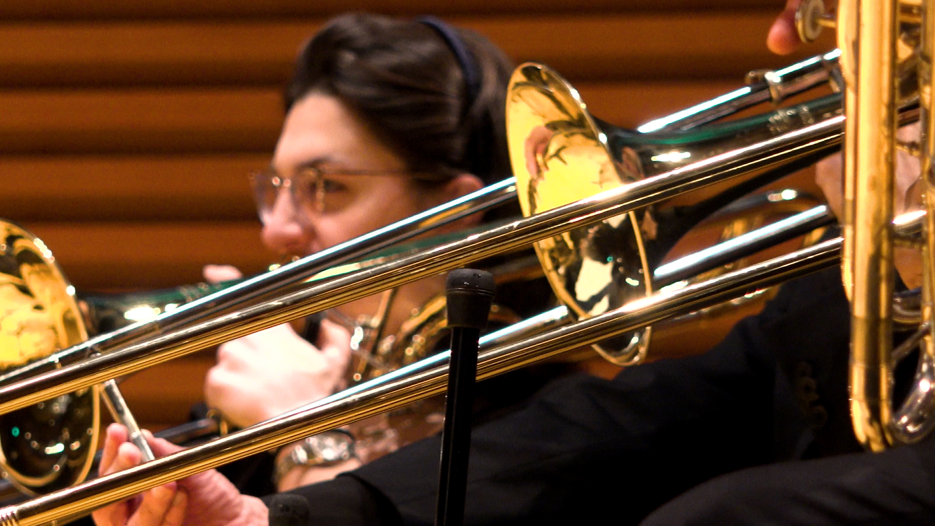 Close-up of two musicians playing brass instruments during a Kansas City Performing Arts performance. One musician's face is partially visible behind the instrument.