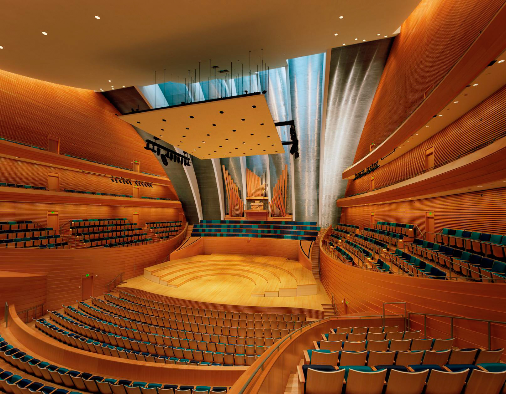 A modern concert hall with a wooden interior, strategically placed lighting, a large stage, and tiered seating arranged in a semi-circular pattern. Seating maps are available to help guests find their perfect spot easily.