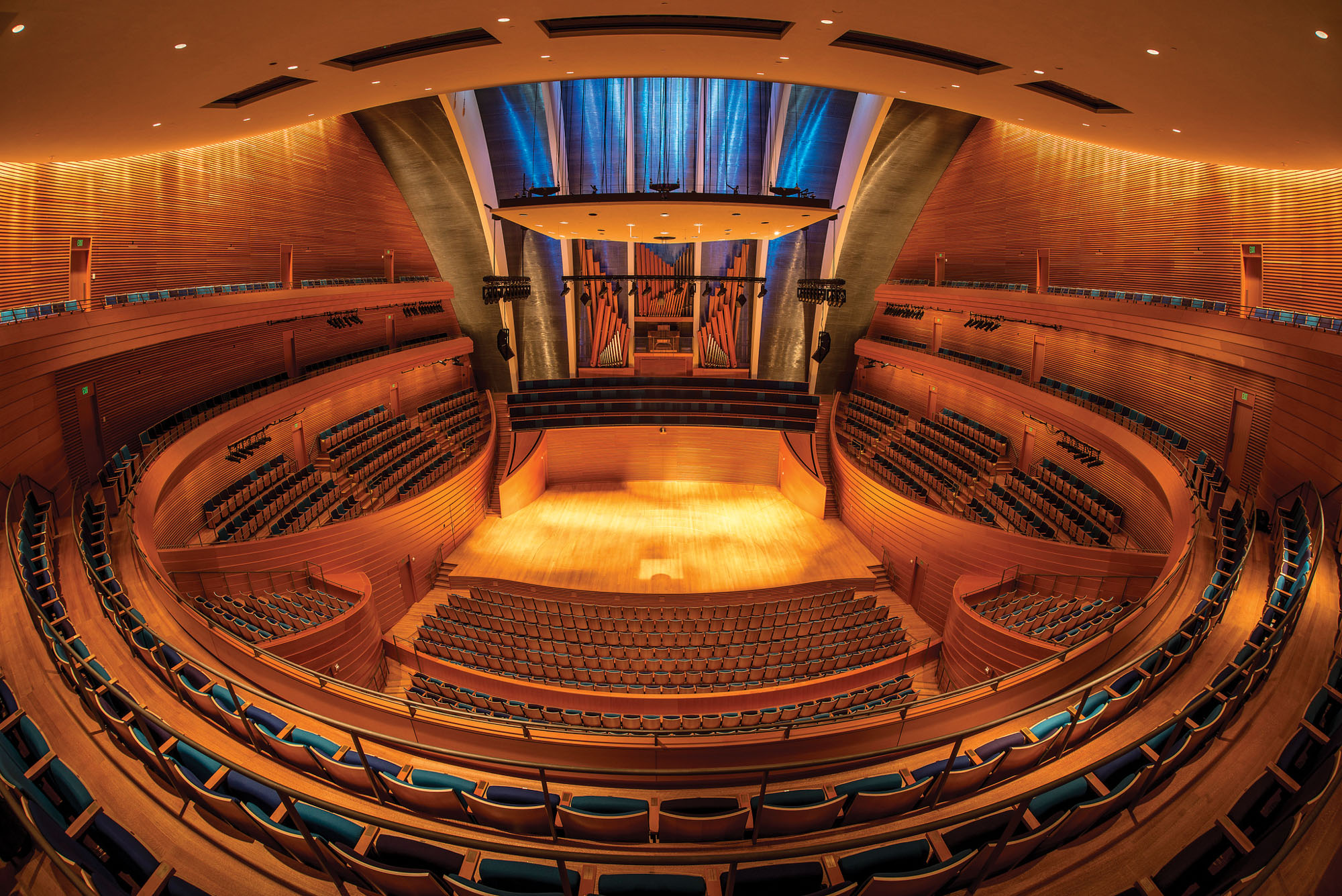 A wide-angle view of an empty, modern concert hall with wooden surfaces, rows of seats, and a stage in the center, perfect for capturing stunning photos and media.