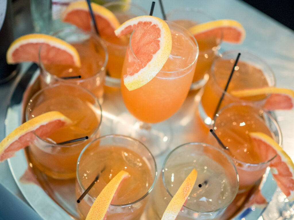 A tray of cocktails garnished with grapefruit slices, each drink containing ice and a black straw.