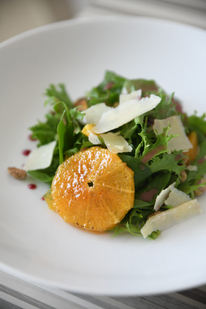 A salad with mixed greens, orange slices, and shaved cheese on a white plate.