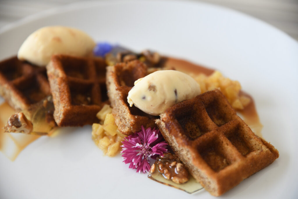 A plate of waffles topped with two scoops of ice cream, garnished with edible flowers, nuts, and a fruit compote.