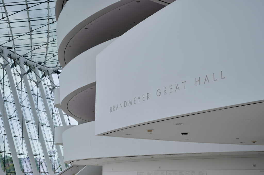 Interior view of spacious Brandmeyer Great Hall featuring curved white balconies and large glass windows.