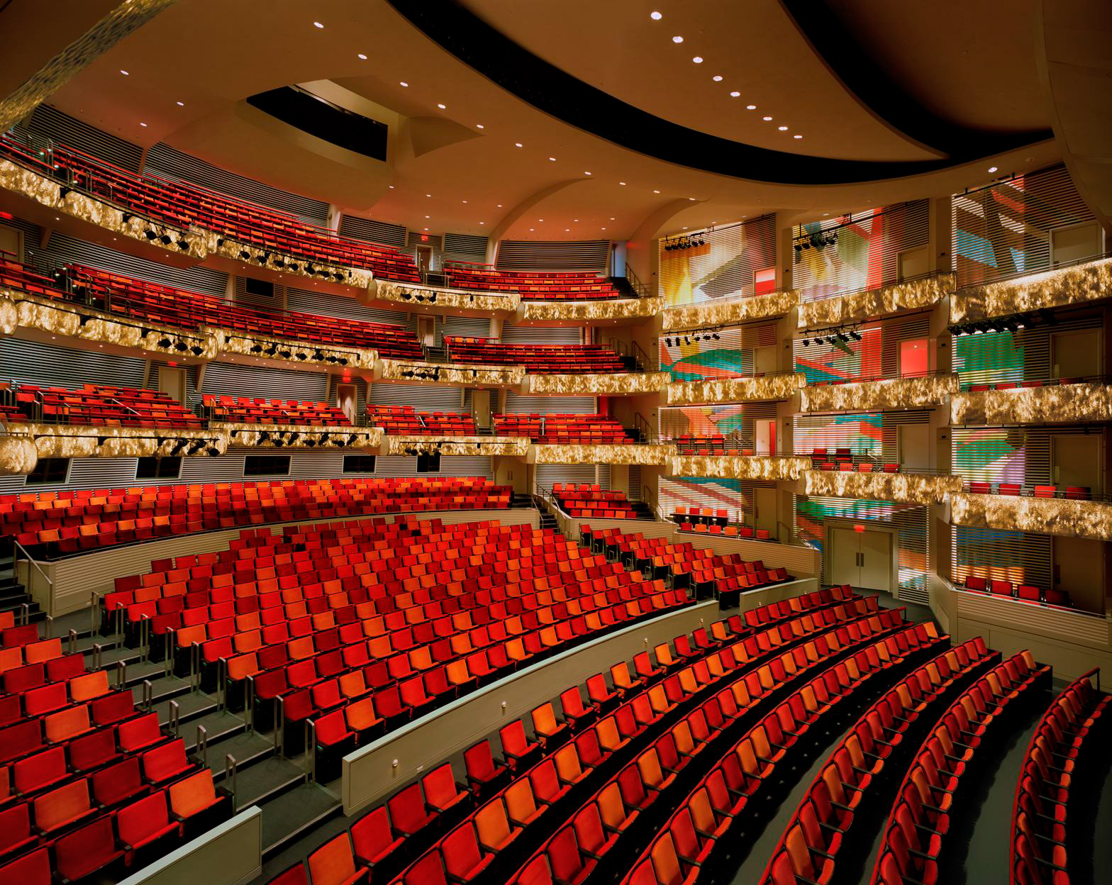 A spacious theater auditorium with multiple tiers of red seating, elaborate gold decor, and modern architecture at the Kauffman Center. This image shows a view from the stage looking towards the seating area, available for rent.