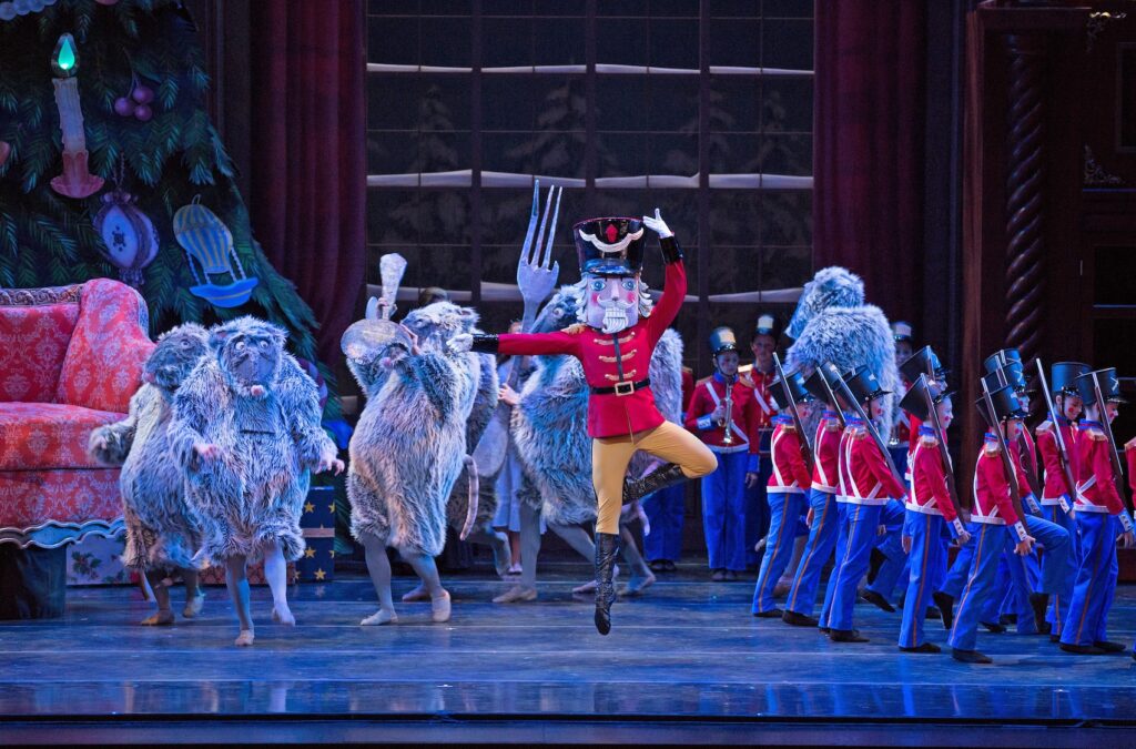 A Performing Arts Sampler showcases a theatrical performance with dancers in animal costumes and toy soldier costumes on stage, featuring a performer in a nutcracker costume mid-jump. A Christmas tree and festive decor adorn the background.