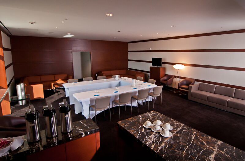 Rent the Kauffman Center's conference room, featuring a U-shaped table setup, chairs, a marble coffee station with cups and carafes, sofas along the sides, and a modern lamp in the corner.