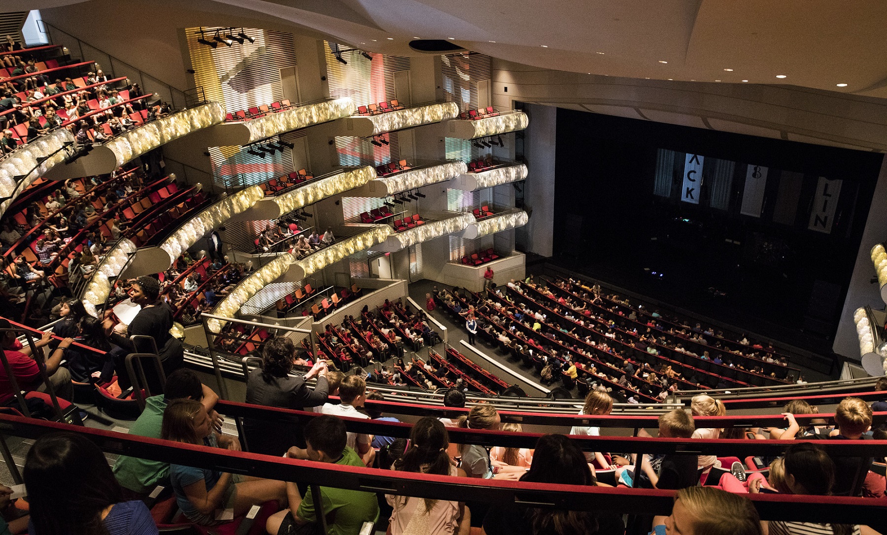 A large auditorium filled with attendees seated in rows before a concert.