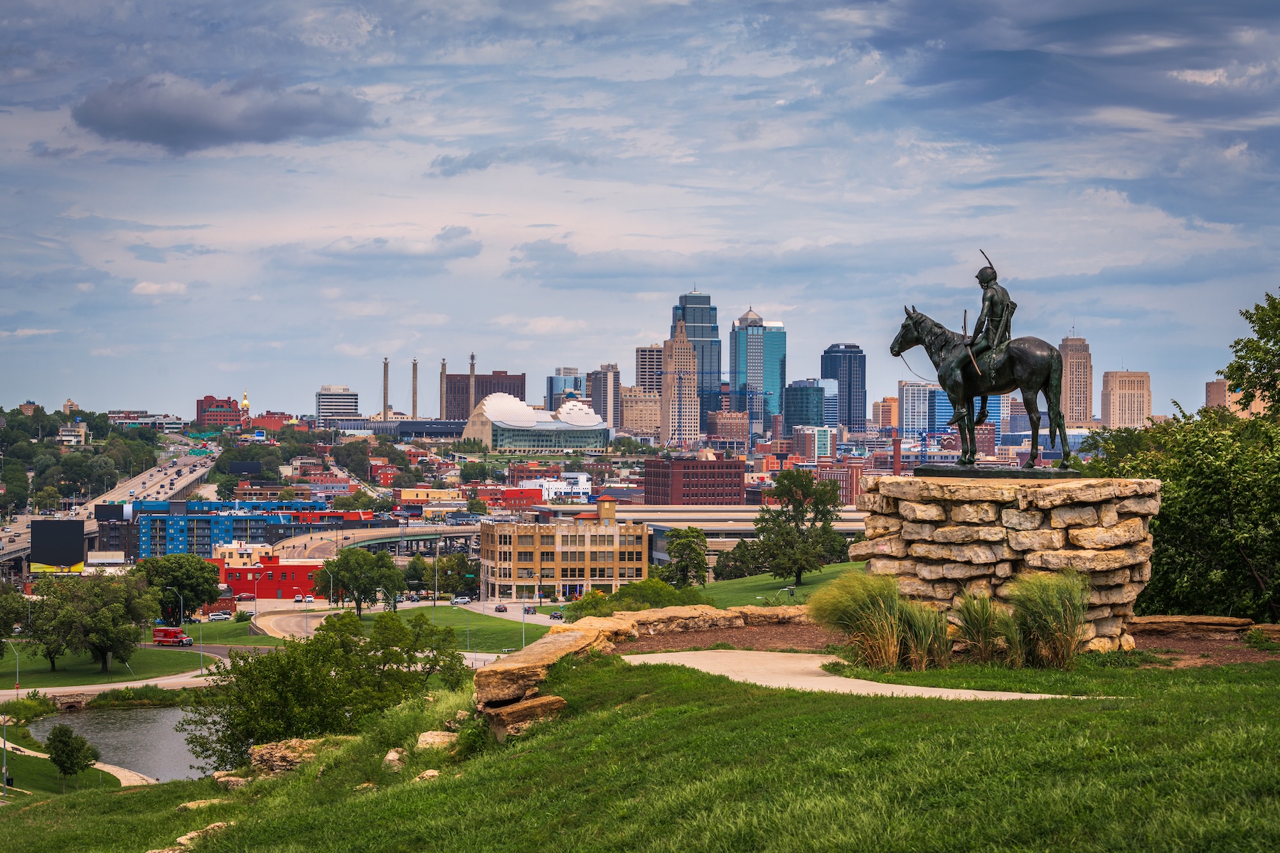 A city skyline with various buildings is seen from a park with a statue of a person on horseback in the foreground, just steps away from dining near Kauffman Center.