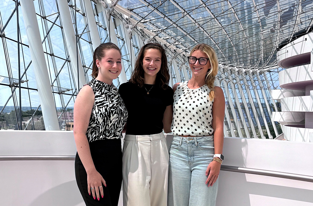 2024 interns stand together smiling inside a modern glass building with a curved ceiling and steel framework, exemplifying our impact for the performing arts.