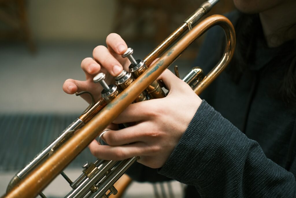 Close-up of a person playing a trumpet, showing their hands pressing the valves on the instrument. The background is blurred, focusing attention on the trumpet and the player's fingers, much like how dining near Kauffman Center offers intimate experiences that highlight culinary details.