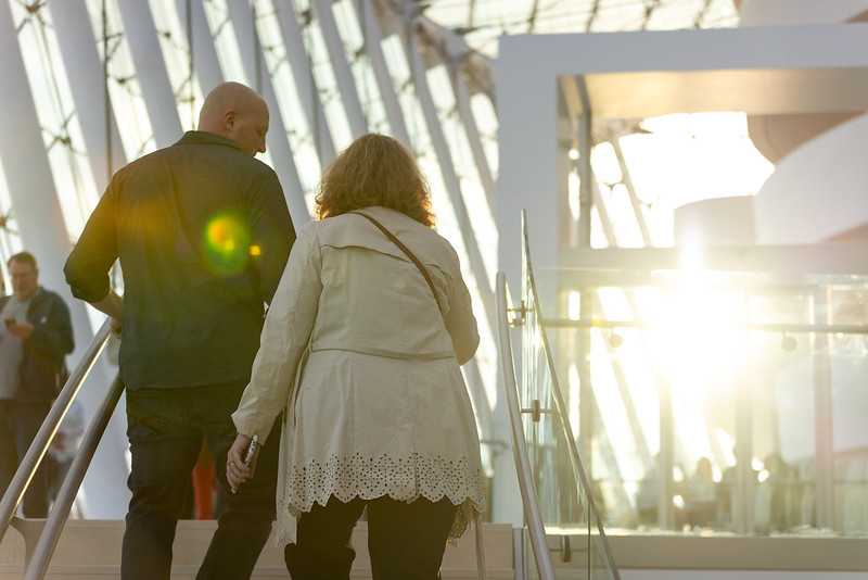 Two people walking up a stairway inside a modern building as sunlight filters through large windows, at sunset