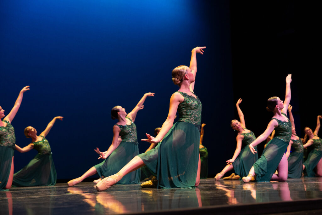 A group of dancers dressed in green costumes perform a ballet routine on stage at the Future Stages Festival. They are in coordinated, graceful poses with arms extended and pointed toes, against a blue-lit backdrop.