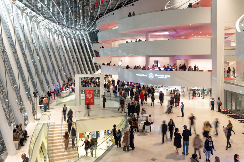 People walking and socializing in the modern, spacious atrium of Kauffman Center with multiple floors, glass walls, and a curved architectural design.