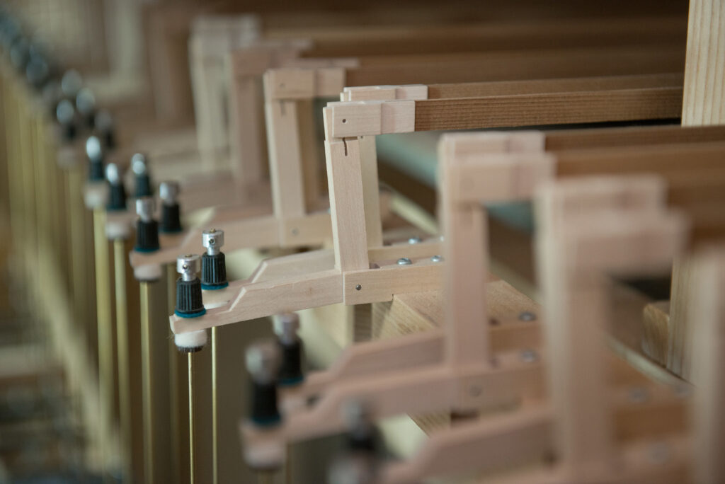 The focus is on the intricate construction and details of the organ, reminiscent of the craftsmanship seen in Julia Irene Dennie-Kauffman Casavant Organ designs. Several wooden pieces and metal knobs are aligned in parallel, with more parts slightly out of focus in the background.