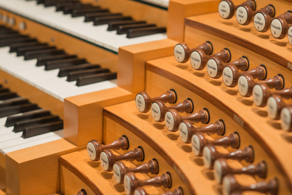 Close-up of the Julia Irene Dennie-Kauffman Casavant Organ console, showing rows of keys and multiple wooden stop knobs with labels. The glossy wooden construction is prominently displayed, highlighting the intricate details and craftsmanship of the instrument.