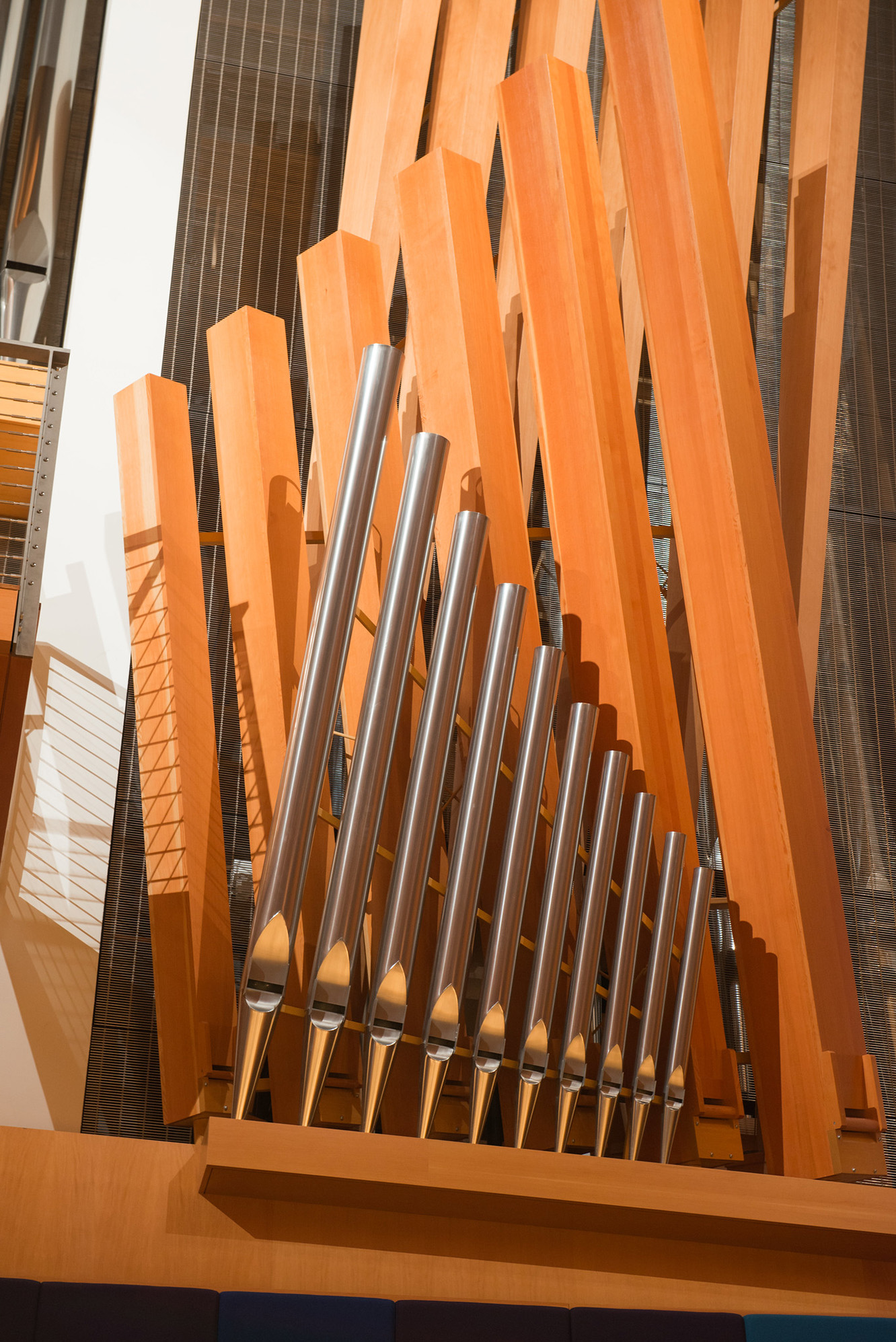 A close-up view of wooden and metallic pipes of the Julia Irene Dennie-Kauffman Casavant Organ, with various sizes of vertical pipes arranged in a row, showcasing the intricate design and craftsmanship. The backdrop features vertical wooden beams and a grid-like structure.